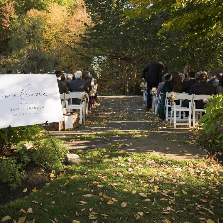 An outdoor ceremony aisle lined with chairs among autumn trees