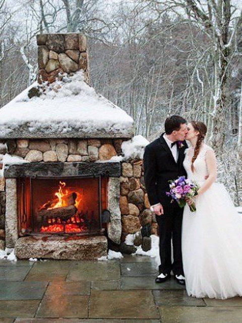 A couple beside the snow-covered stone fireplace patio at Harrington Farm